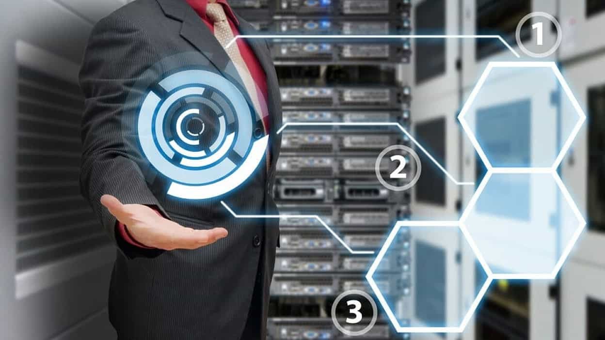 Businessman in a suit in a server room holding out his hand with blue technology graphics above it