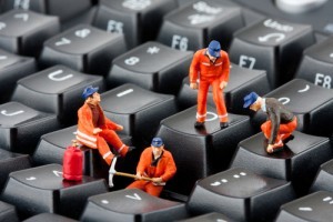 Black keyboard with little figures in orange suits and blue hats on it working